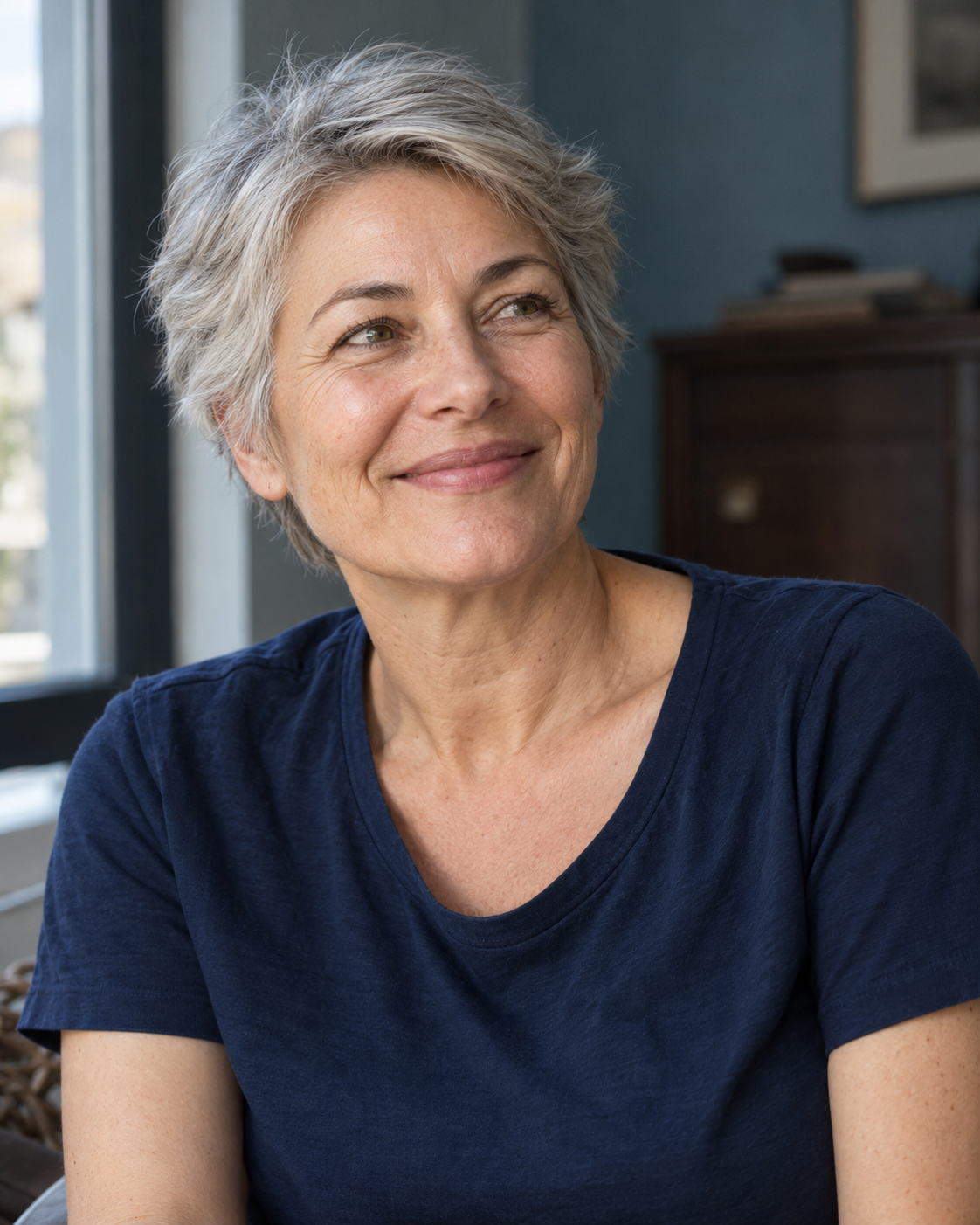 Portrait d’une femme aux cheveux courts argentés, en tee-shirt bleu marine, regard tourné hors champ.